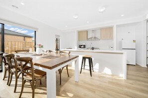 A modern kitchen with a central island, wooden chairs, and a large dining table.