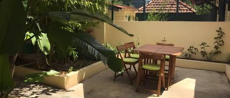 A patio with a table and chairs, surrounded by greenery and a white canopy.
