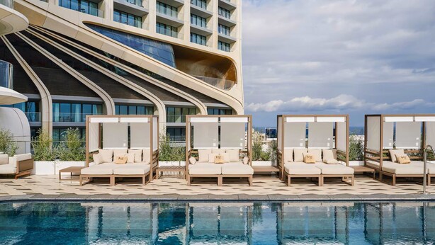 Un hôtel moderne doté d’un espace piscine avec des chaises longues et d’un grand bâtiment à la façade incurvée originale.