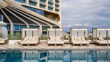 A modern hotel with a pool area featuring lounge chairs and a large building with a unique curved facade.