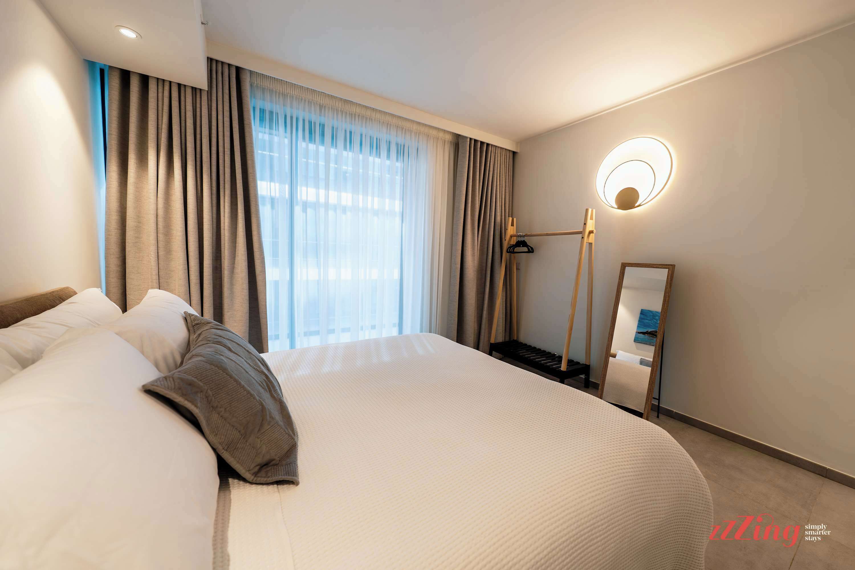 Une chambre d’hôtel avec un grand lit, une table de chevet, un miroir et un luminaire fixé au mur.