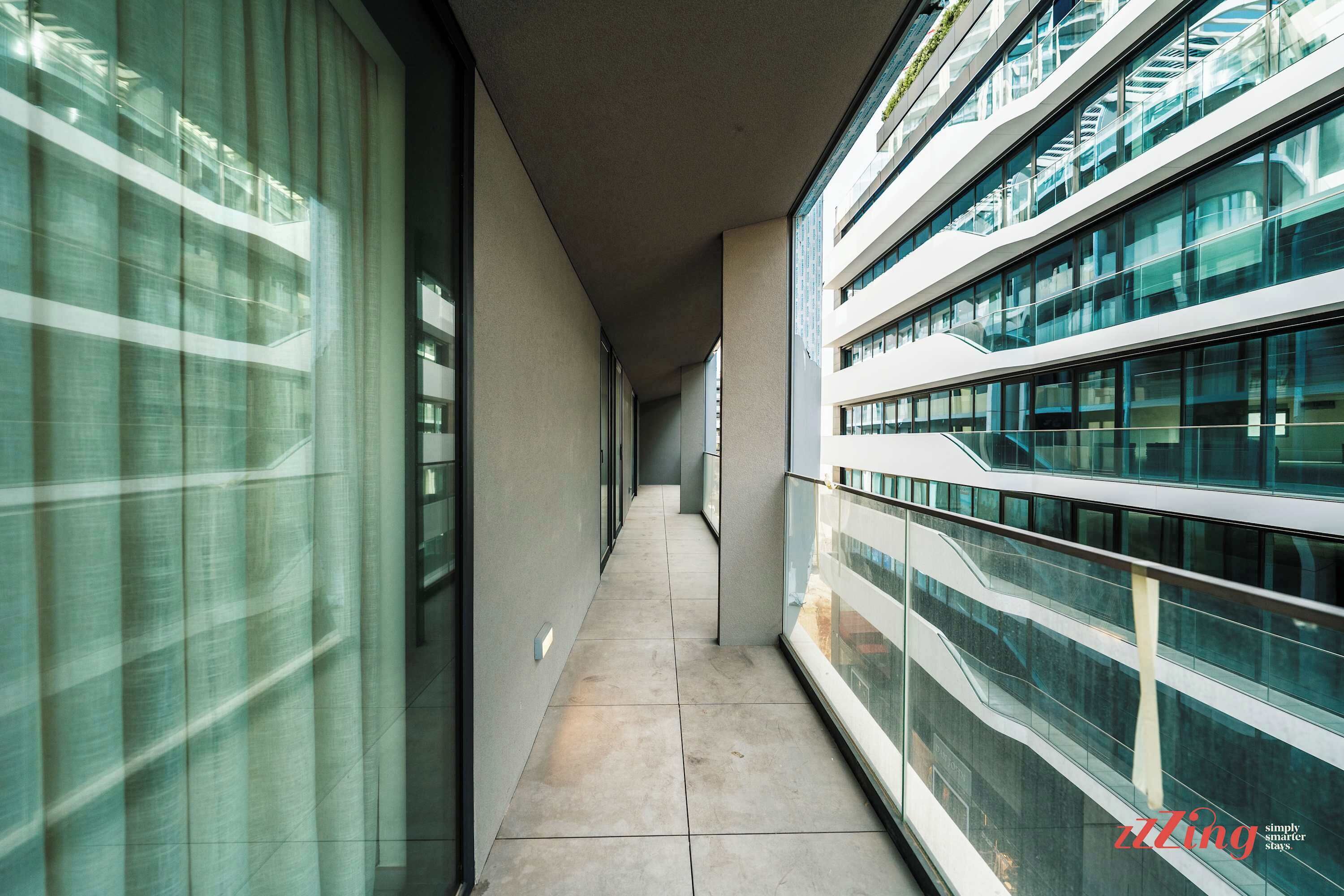 A corridor with glass railings and a tiled floor, leading to a modern building with multiple floors.