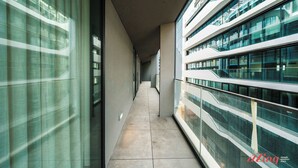 Un couloir doté de rampes en verre et d’un sol carrelé, qui mène à un bâtiment moderne à plusieurs étages.