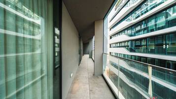 A corridor with glass railings and a tiled floor, leading to a modern building with multiple floors.