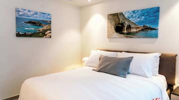 A bedroom with a large bed, two paintings of coastal scenes, and a nightstand with a lamp.