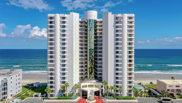 A high-rise hotel with multiple balconies, a central cylindrical structure, and a view of the ocean.