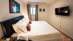 Hotellihuone, jossa on sänky, taulutelevisio, ikkuna verhoilla ja taulu seinällä.