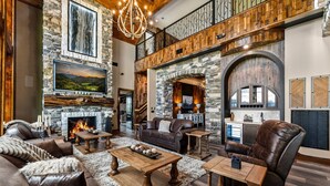 Un salón amplio con chimenea de piedra, muebles de cuero y un techo alto con vigas a la vista.