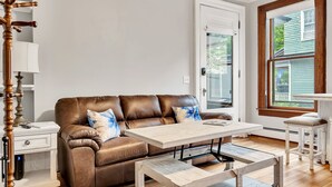 Un salón acogedor con un sofá de cuero marrón, una mesa de centro de madera y una mesita auxiliar blanca.
