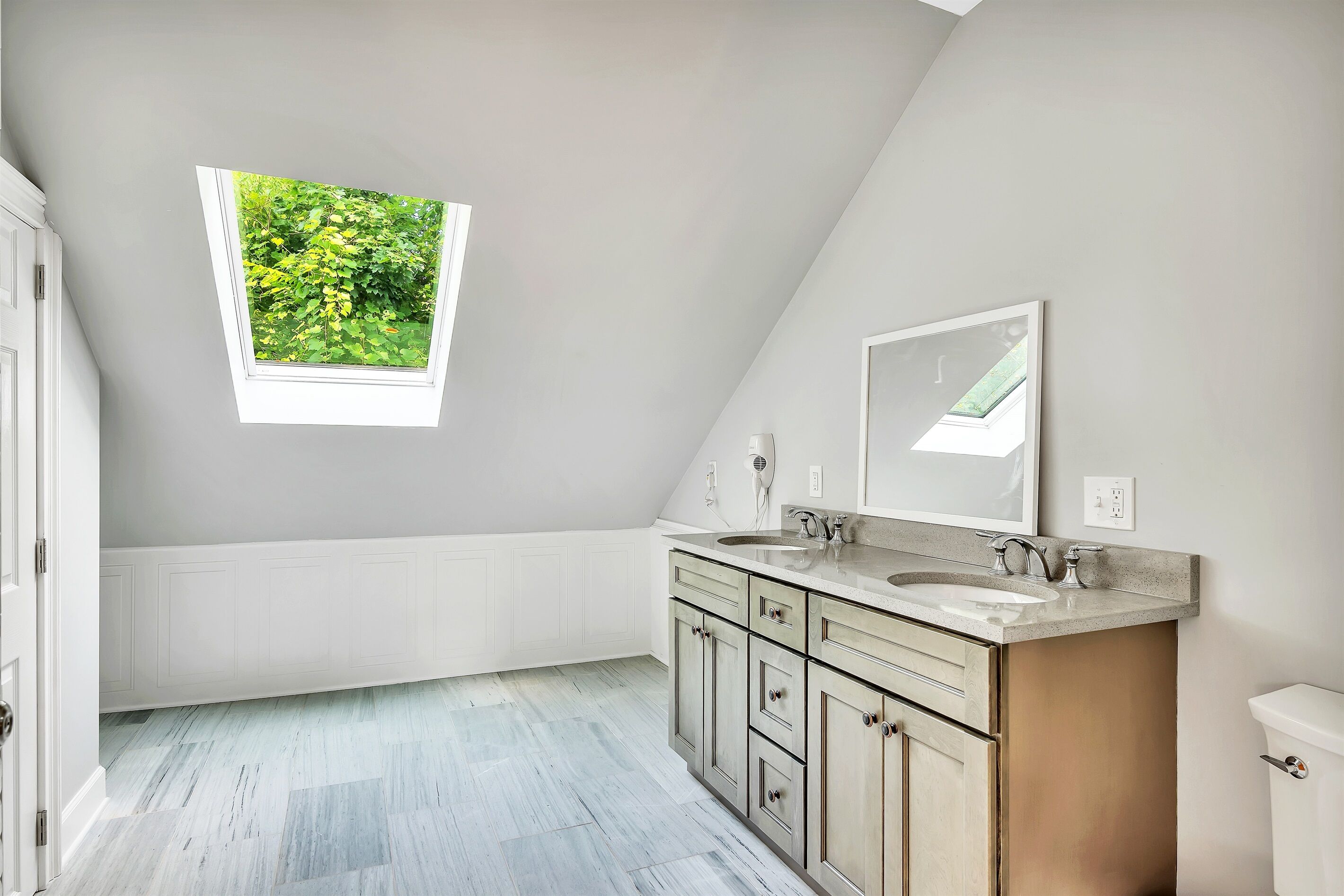 Un bagno con finestra sul tetto, due lavandini e un water.