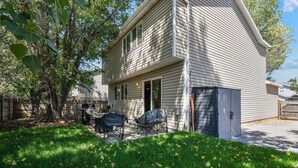 Een tweelaags huis met een overdekte patio, een barbecue en een tuinhuis.