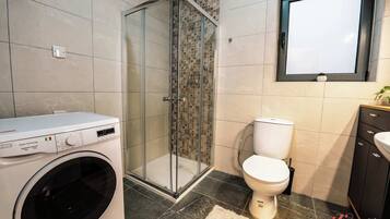 Un baño moderno con lavadora, cabina de ducha con vidrio, inodoro y lavamanos.