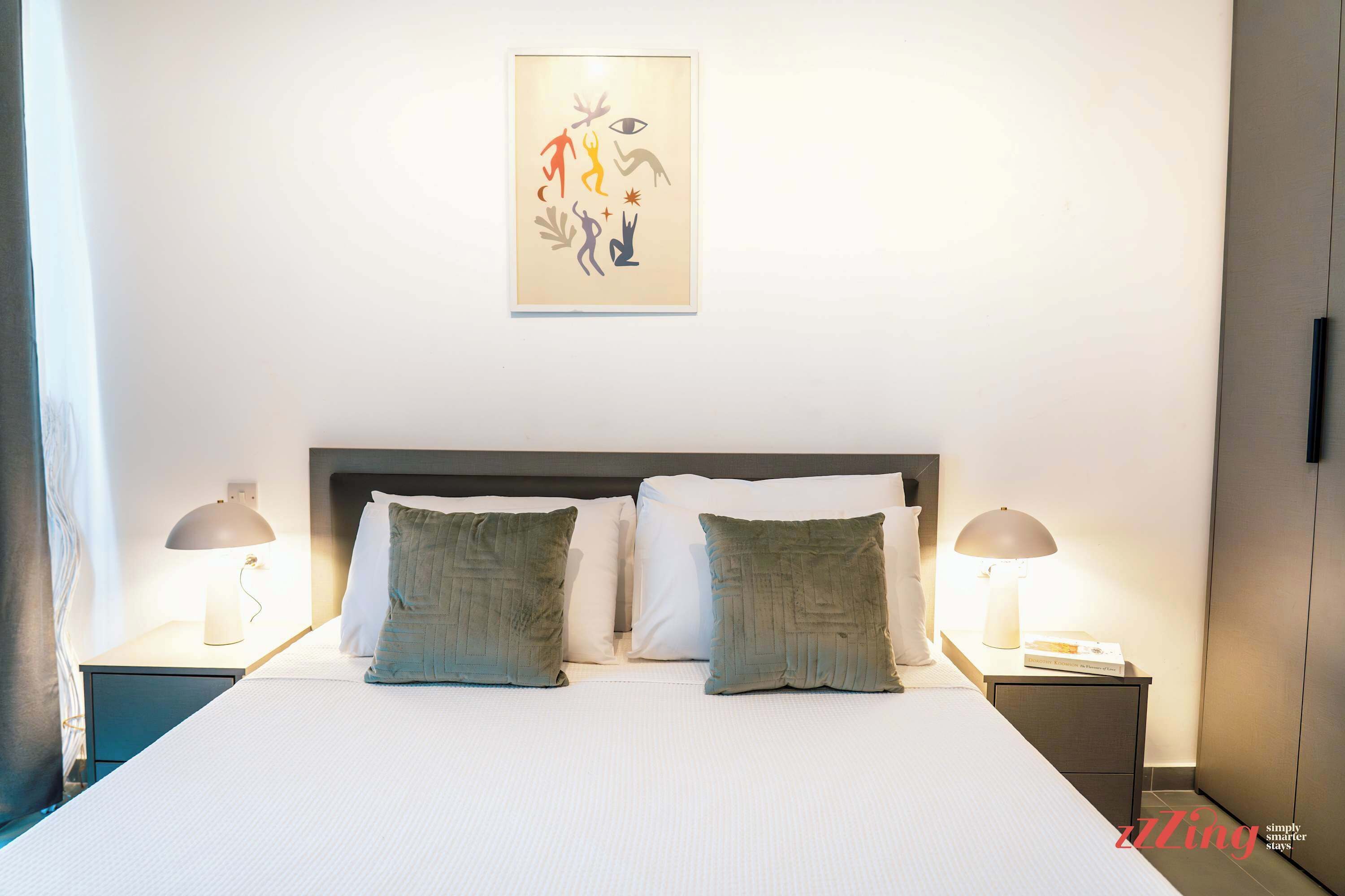 Habitación de hotel impecable con una cama grande, dos mesitas de noche con lámparas y una obra de arte colgada en la pared.