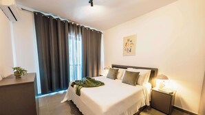 A hotel room with a large bed, a bedside table, a lamp, a wall art piece, and a window with curtains. - Msida's Most Loved Stylish Duplex Retreat (Tal-Pietà)