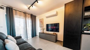 A modern living room with a dark sofa, a flat-screen TV, and a minimalist design. - Msida's Most Loved Stylish Duplex Retreat (Tal-Pietà)