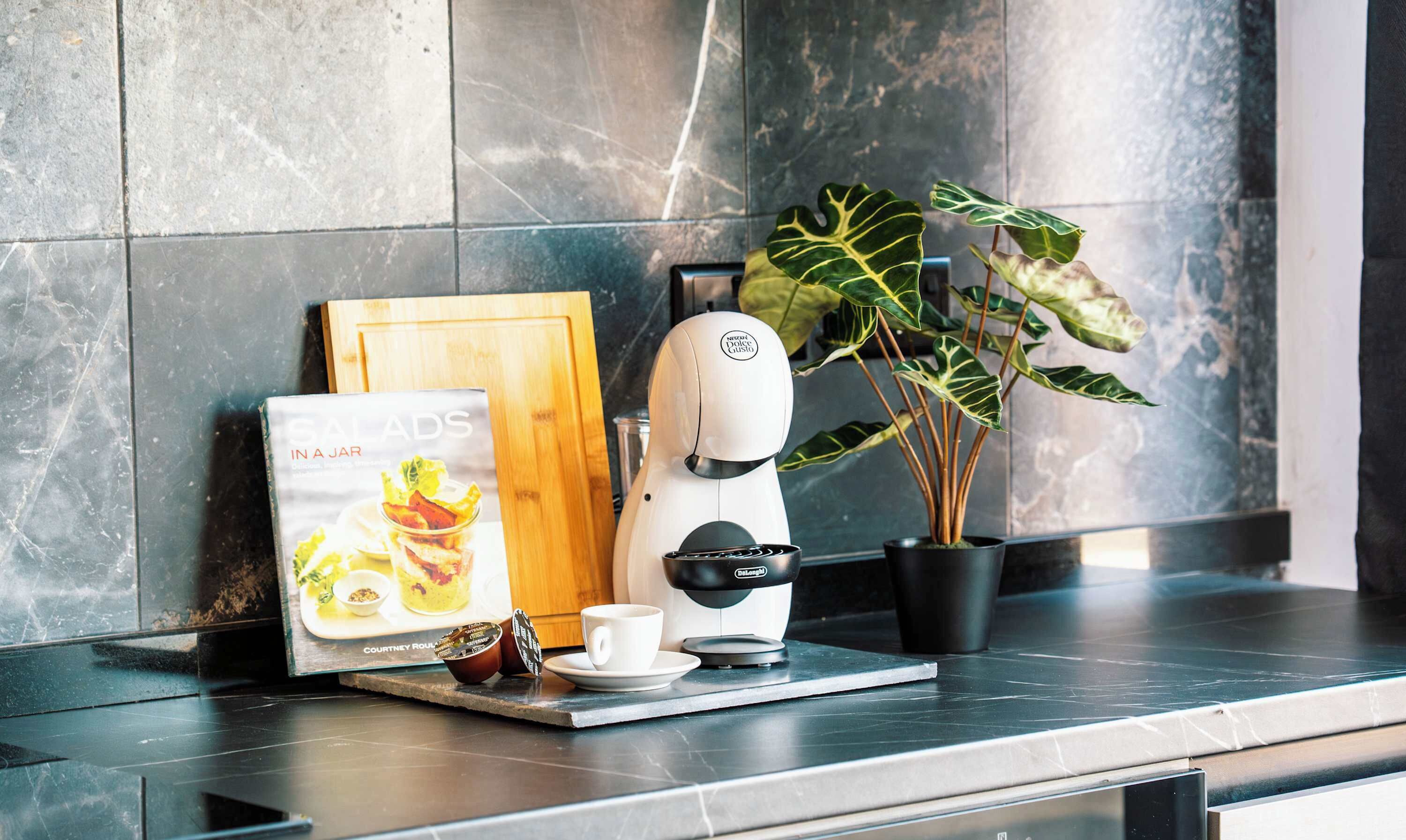 Een moderne keuken met een koffieapparaat, een kookboek, een potplant en een houten snijplank.