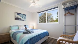 A bedroom with a bed, a bedside table, a chair, a window, and a ceiling fan.