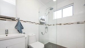 A modern bathroom with a glass shower enclosure, a toilet, and a sink with a towel hanging on the wall.