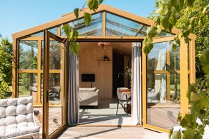 A modern glass house with a wooden deck, a sofa, and a TV. - Holiday Home in Scherpenzeel (Scherpenzeel)