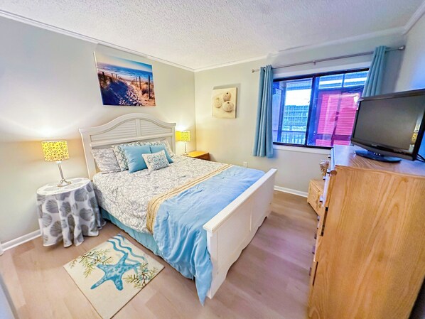 Une chambre à coucher avec un lit, des lampes de chevet, un téléviseur et une fenêtre avec des rideaux.