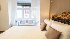 Une chambre d’hôtel avec un grand lit, une tête de lit au décor travaillé, une fenêtre avec des rideaux et une vue sur un bâtiment à l’extérieur.