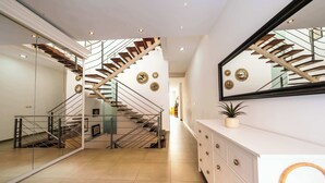 Un intérieur moderne avec un escalier, un mur miroir et une commode blanche.