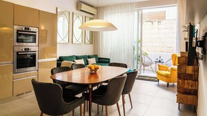Une cuisine moderne dotée d’appareils électroménagers intégrés, un coin repas avec une table et des chaises en bois, un canapé et un fauteuil jaune.