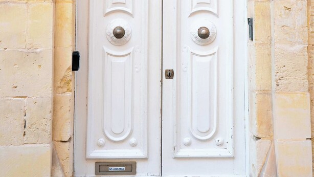 Une porte double blanche, surmontée d’une arche décorative, est encastrée dans un mur de pierres jaunes.
