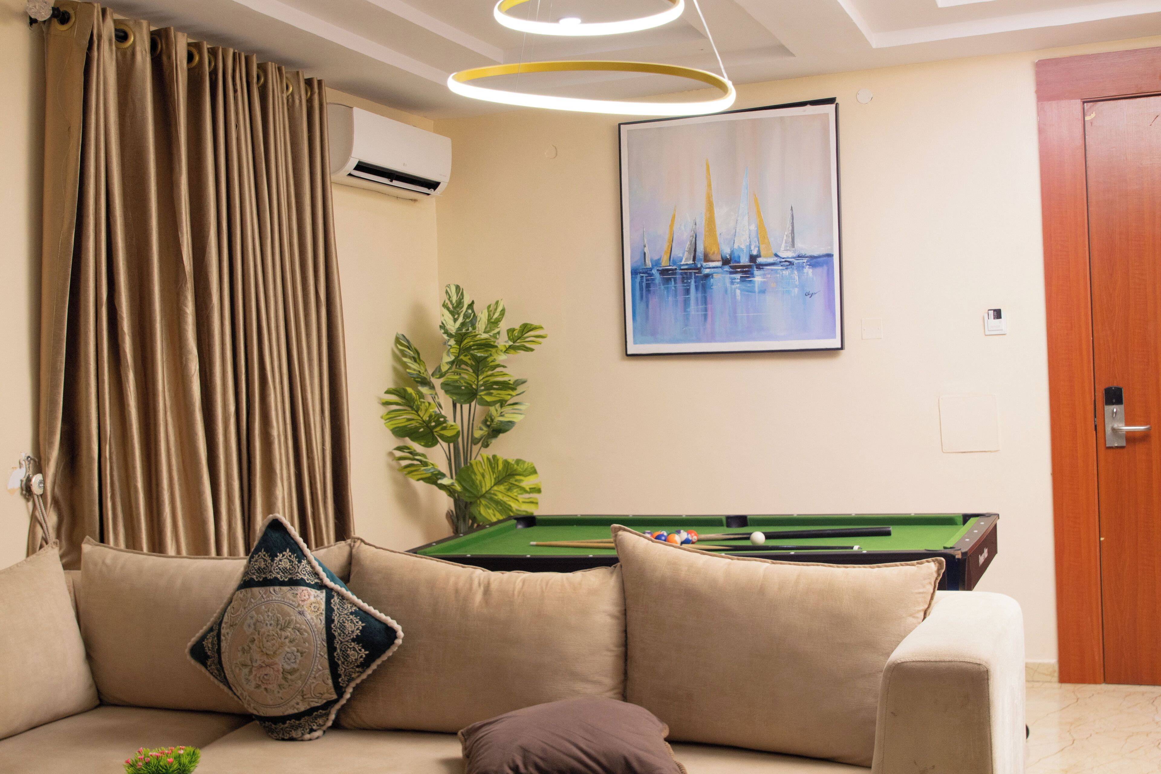 A living room with a pool table, a sofa with decorative pillows, a potted plant, and a painting on the wall.