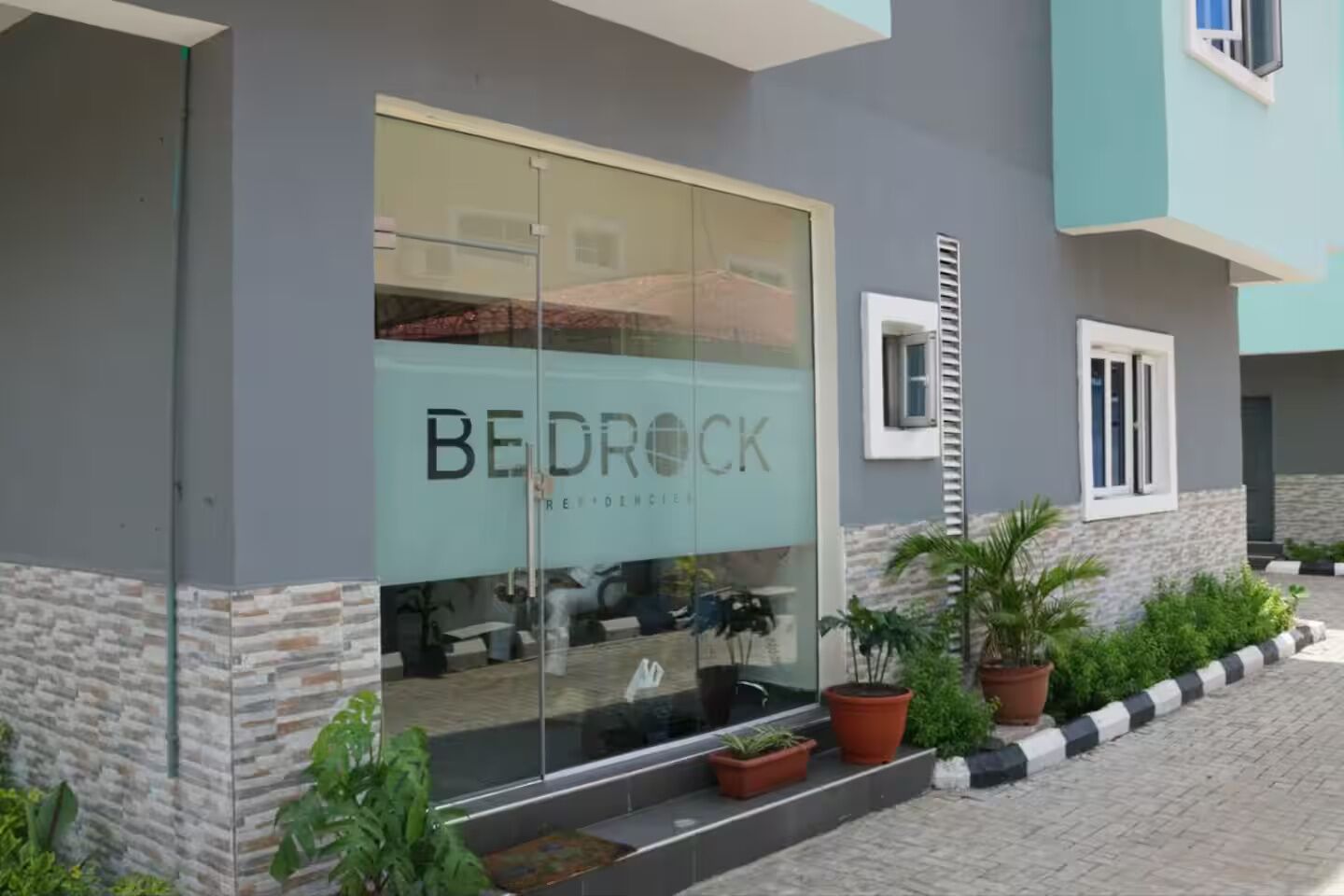 Un edifici modern amb una gran façana de vidre, un rètol que diu "BEDROCK Residences" i una exterioritat de pedra i totxana.