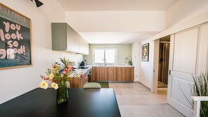 Eine moderne Küche mit einer zentralen Kochinsel, einem Essbereich mit schwarzem Tisch und einer Blumenvase sowie Blick auf den angrenzenden Wohnraum.