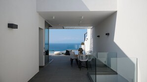 Ein moderner Balkon mit Glasgeländer, einem Esstisch mit Stühlen und Blick aufs Meer.