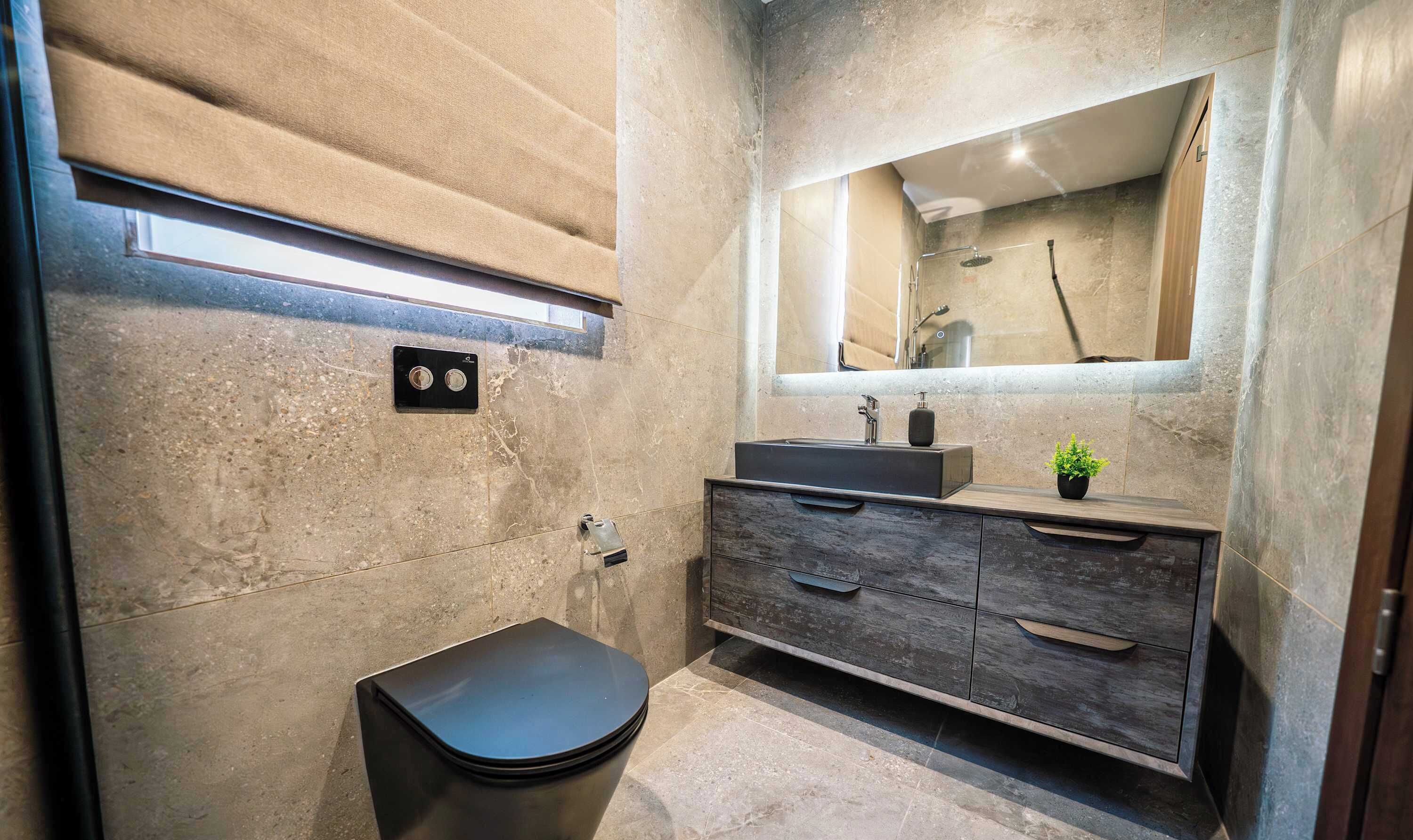 Een moderne badkamer met een grote spiegel, een zwart toilet, een houten wastafelmeubel en een kleine plant.