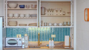 A kitchen with a microwave, sink, and shelves with dishes and glasses. - Beachfront Condo w/ Stunning Ocean Views (Hauula)