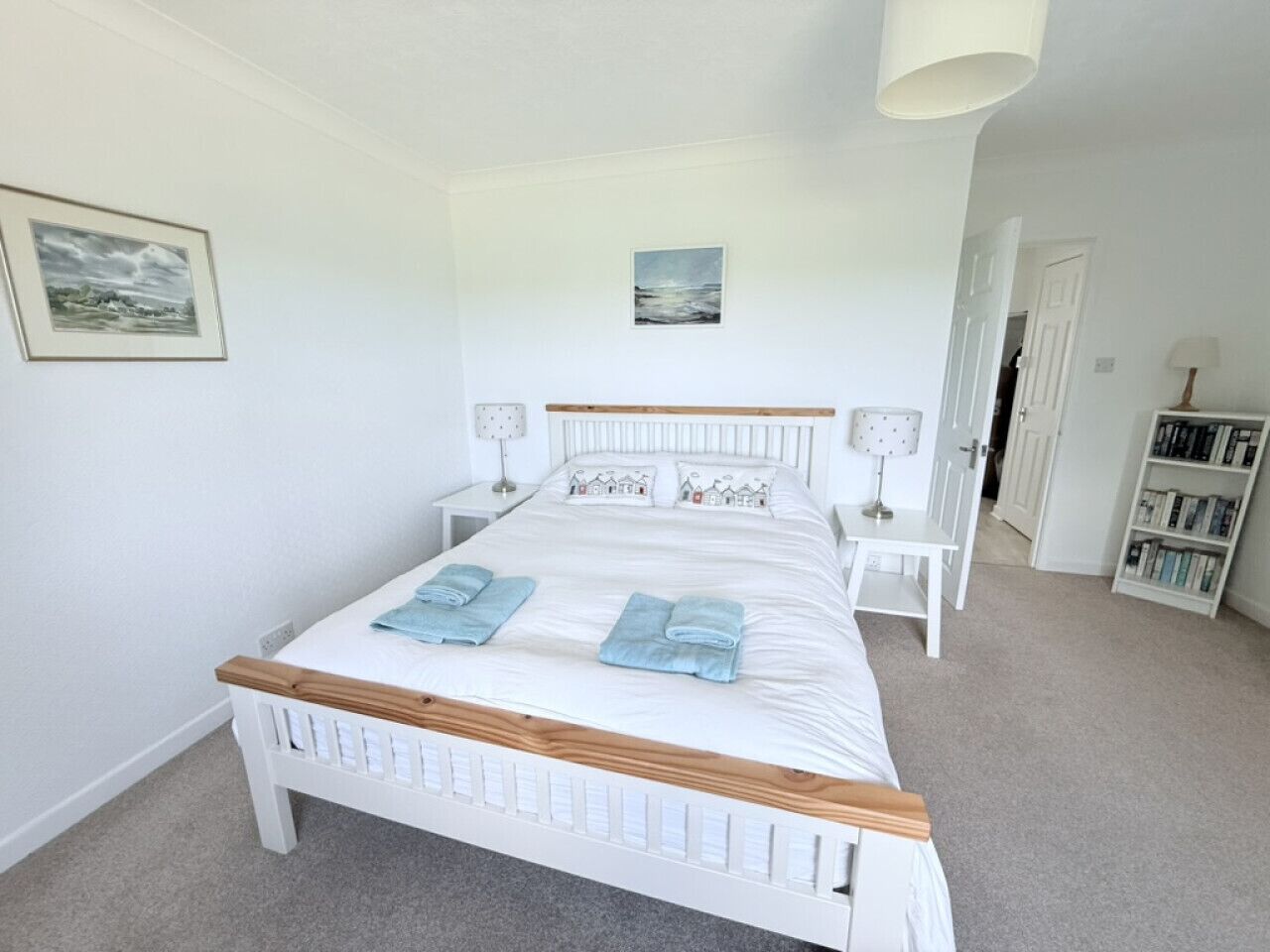 A neatly arranged bedroom with a bed, bedside tables, a bookshelf, and a door.