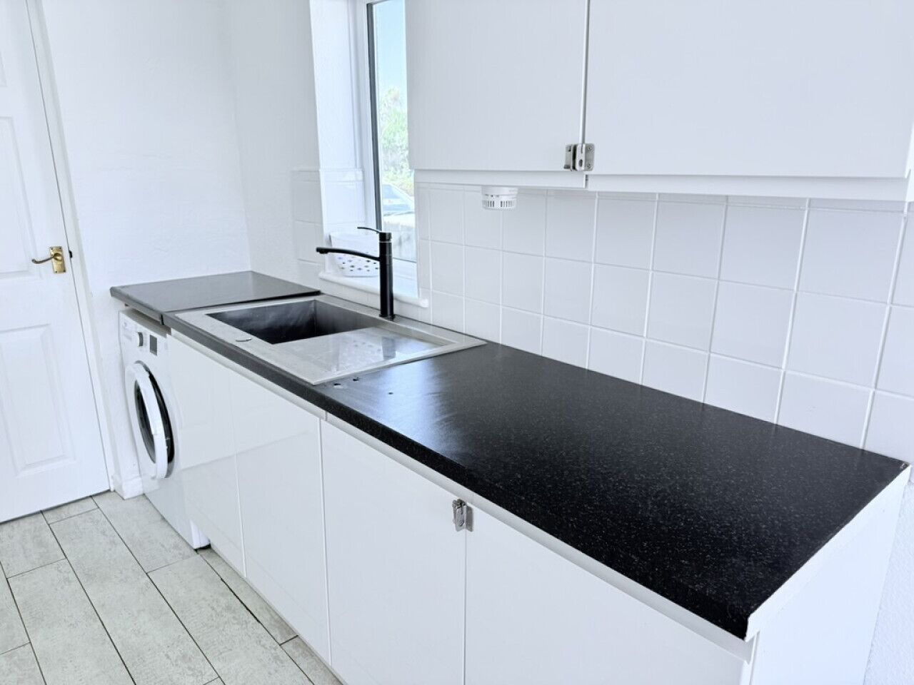 Een keuken met witte kastjes, een zwart aanrecht, een ingebouwde wasmachine en een raam boven de gootsteen.