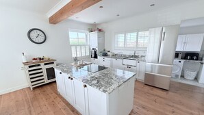 Une cuisine spacieuse avec des meubles blancs, un îlot central doté d’un plan de travail en marbre et un revêtement de sol en bois.