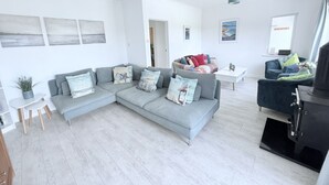 Un salon moderne avec un canapé d’angle gris, une petite table blanche et une cheminée noire.