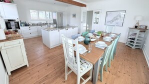 Une cuisine spacieuse avec des meubles blancs, un îlot central et un coin repas comprenant une table et des chaises en bois.