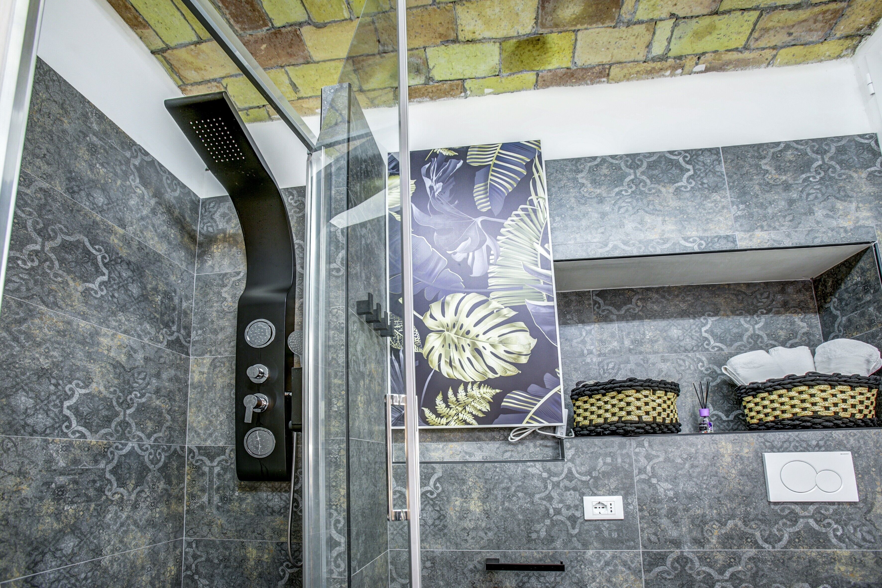 Dusche mit Glasabtrennung, ein Wandhandtuchhalter und ein dekoratives Blattmuster-Panel.