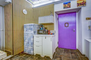 Una cocina con microondas, tetera y armarios, una puerta morada y un respuesto de azulejos.