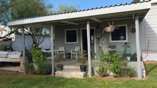 A covered porch with two white chairs, a small table, and a birdcage.