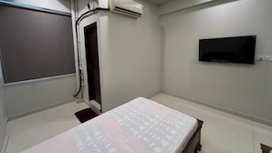 A hotel room with a bed, a flat-screen TV mounted on the wall, an air conditioning unit, and a window with a view. - Prestige Comfort Apartments Separate Lounge With Newly Bath With Reception (Karachi)