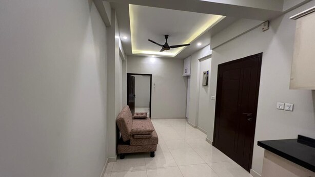 A hallway with a sofa, a ceiling fan, and a door. - Prestige Comfort Apartments Separate Lounge With Newly Bath With Reception (Karachi)