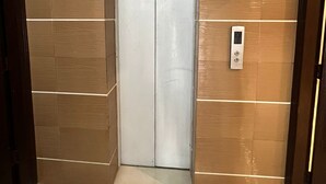 A narrow elevator with a control panel on the wall, surrounded by brown tiles. - Prestige Comfort Apartments Separate Lounge With Newly Bath With Reception (Karachi)