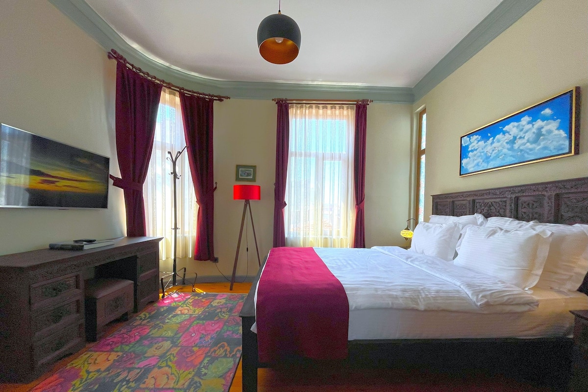 A hotel room with a bed, a desk, a television, and a colorful rug.