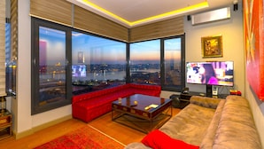 A modern living room with large windows, a red sofa, a coffee table, and a television. - Flex O'pera Hotel (Istanbul)
