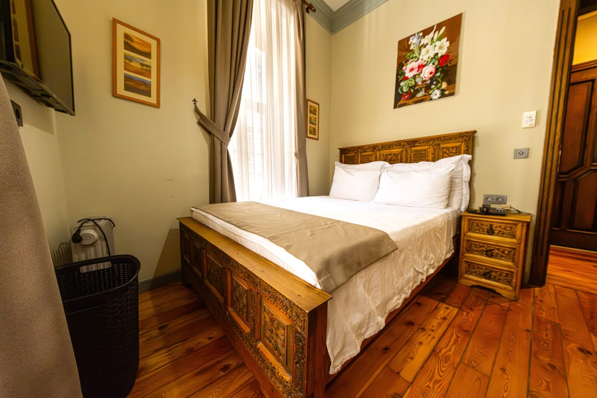 A bedroom with a wooden bed, a nightstand, a radiator, and a framed painting on the wall.