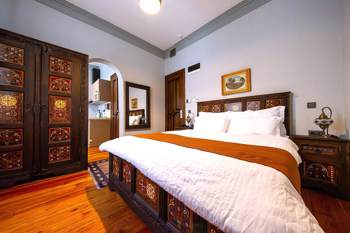 A bedroom with a large bed, wooden wardrobe, and a mirror.