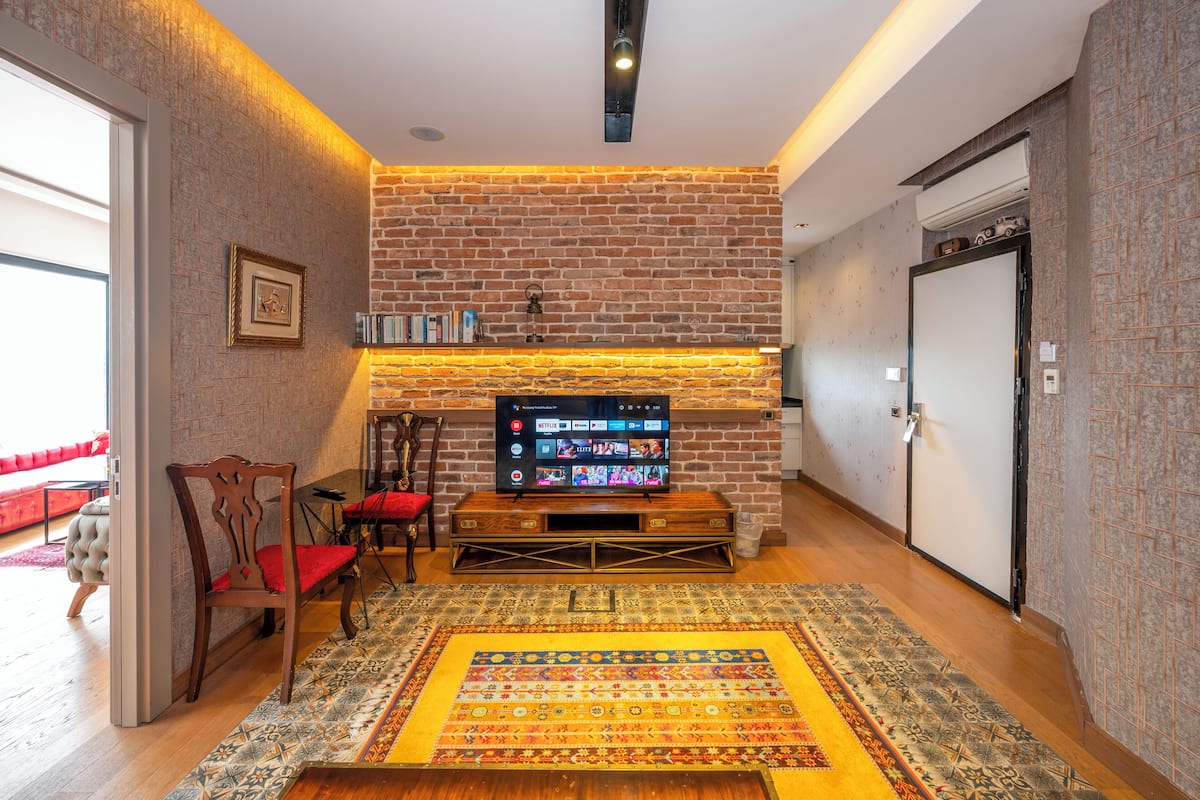 A living room with a brick wall, a fireplace, a television, and a patterned rug.